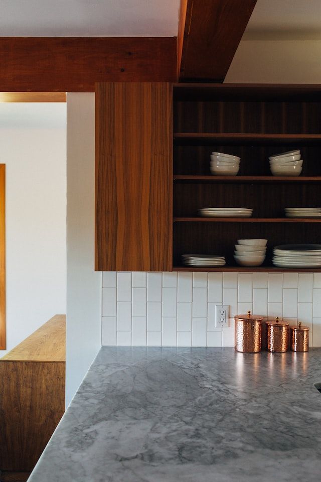 A kitchen with a marble counter top , wooden cabinets , and copper canisters.