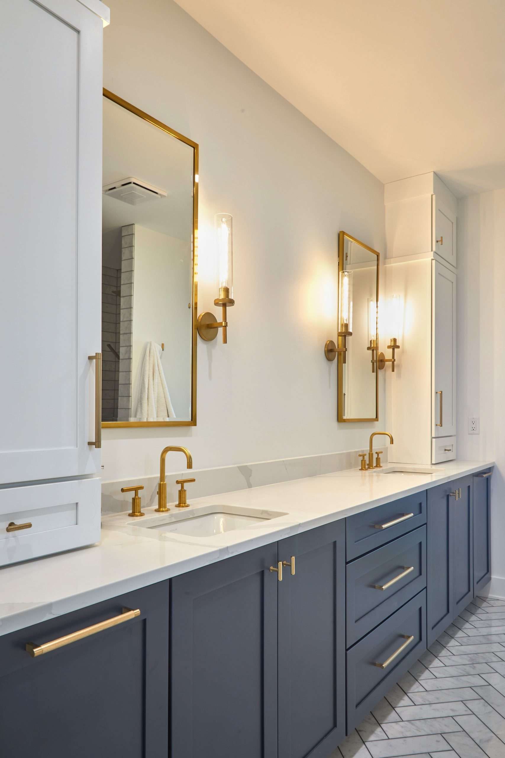 A bathroom with two sinks , two mirrors , and blue cabinets.