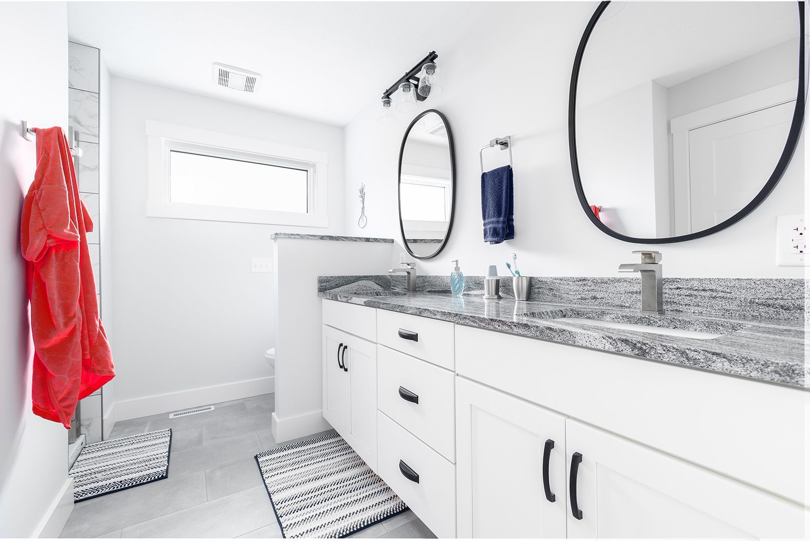 A bathroom with two sinks , a mirror and a red towel hanging on the wall.