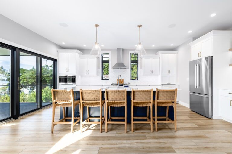 A kitchen with white cabinets , stainless steel appliances , wicker chairs and a large island.