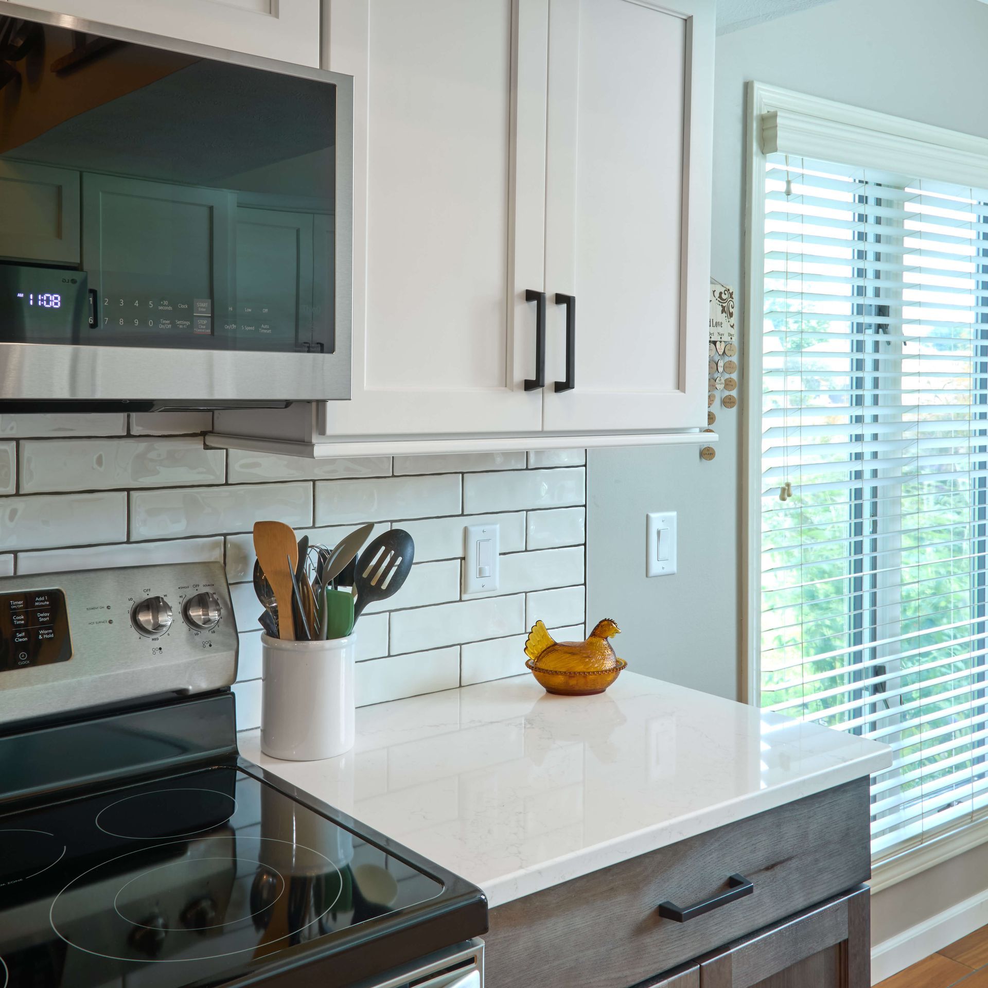 White kitchen with white and gray cabinets, a white countertop, and a window with blinds.
