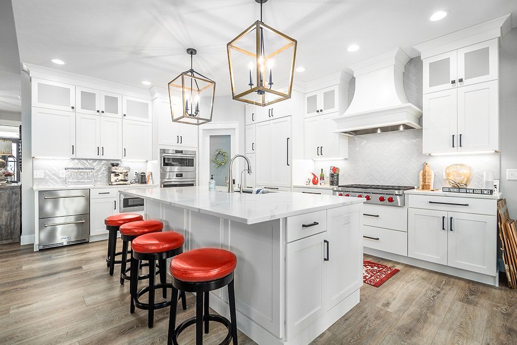A kitchen with white cabinets , red stools and a large island.