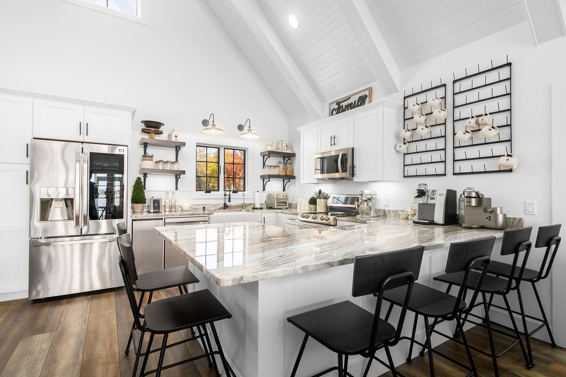 A kitchen with white cabinets , stainless steel appliances , granite counter tops and black chairs.