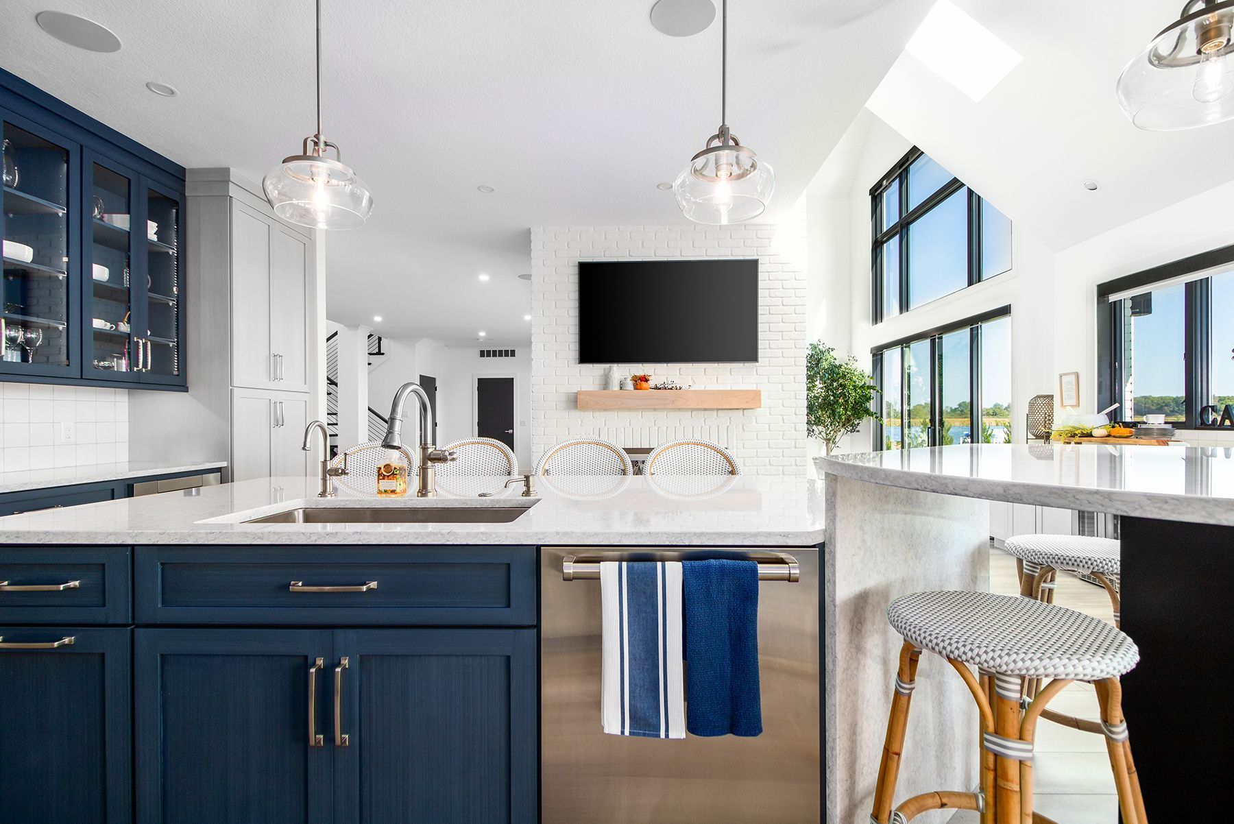 A kitchen with blue cabinets , a sink , a stainless steel dishwasher and a flat screen tv.