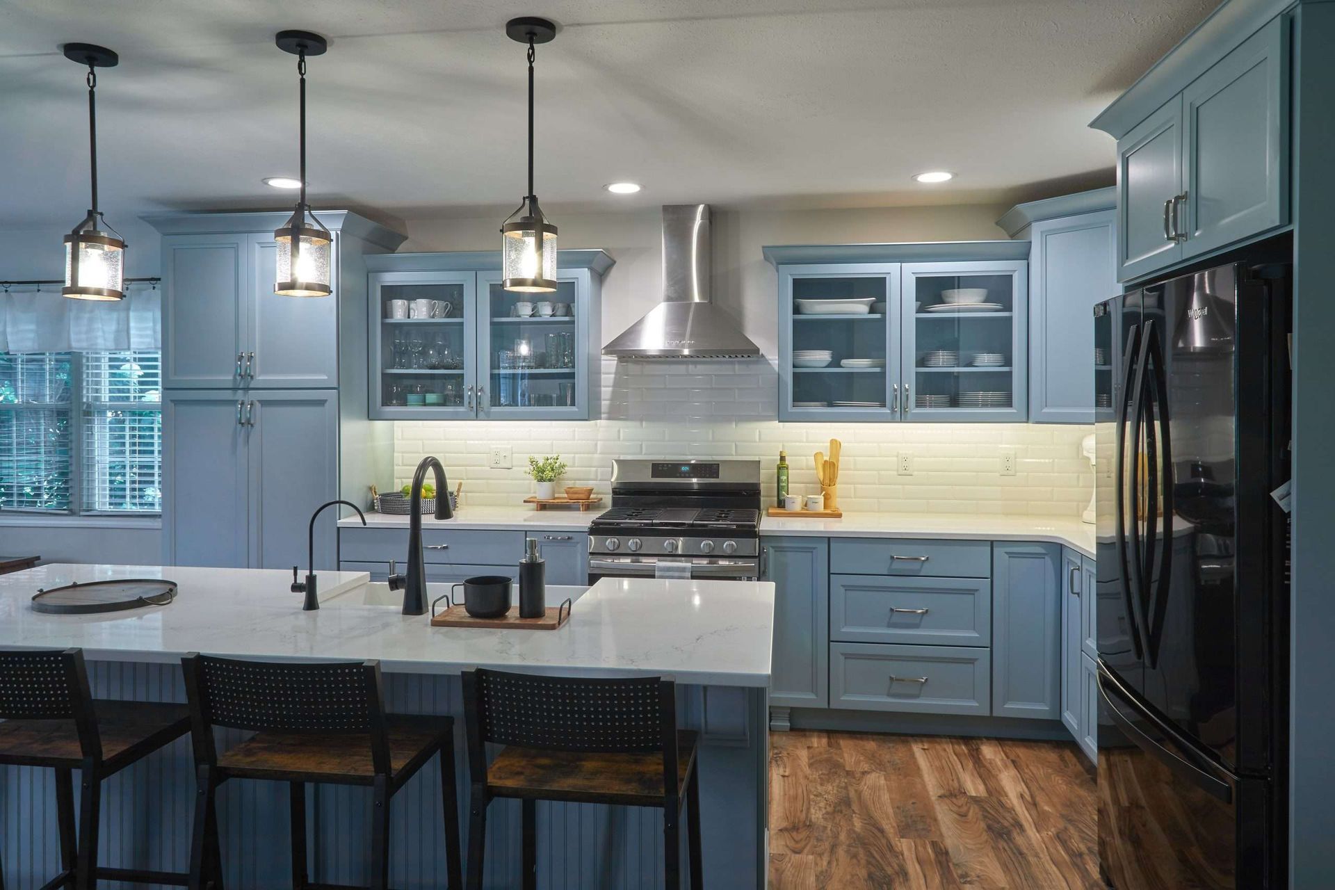 A kitchen with blue cabinets , white counter tops , stainless steel appliances and a large island.