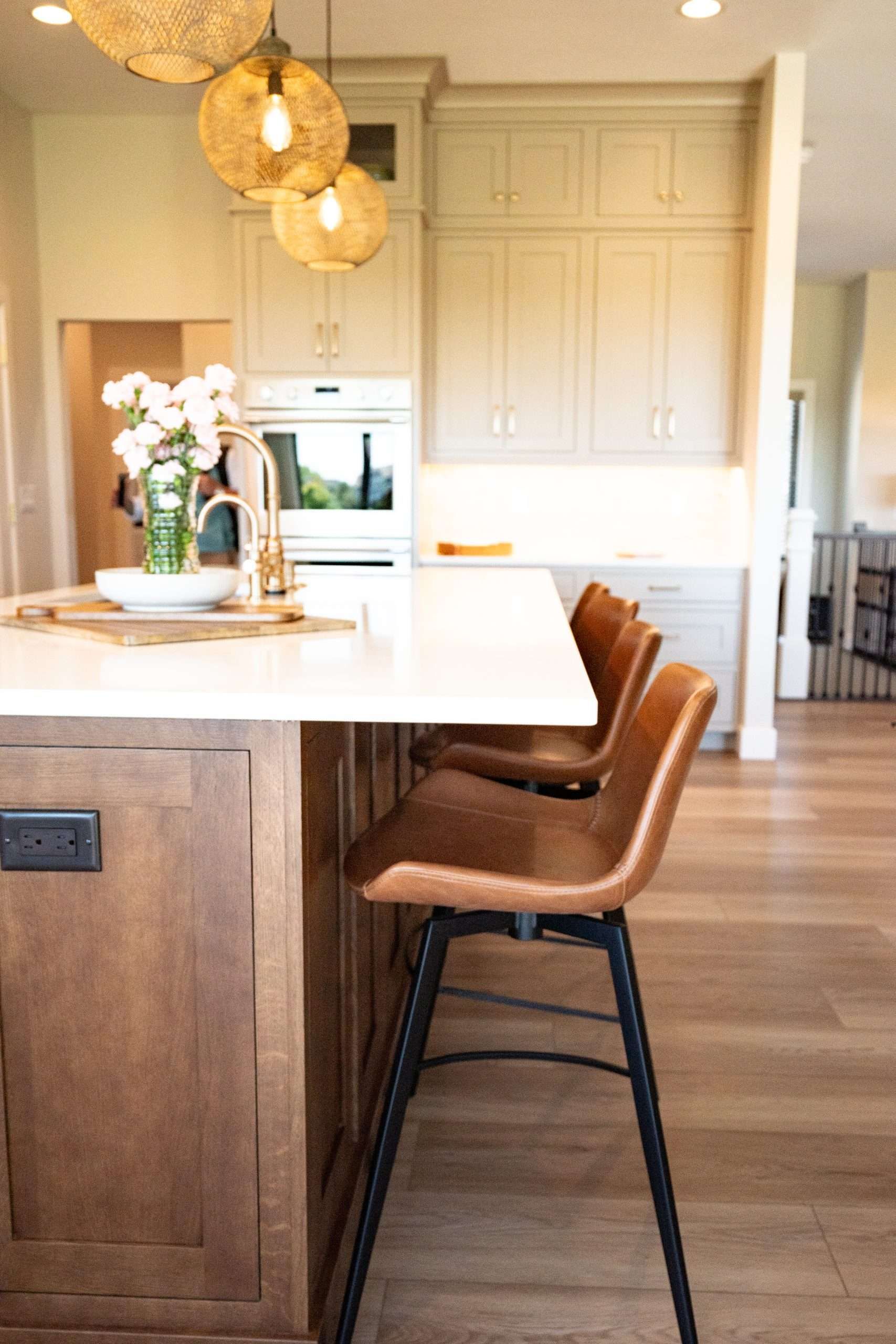 A kitchen with a large island , stools and a vase of flowers on the counter.