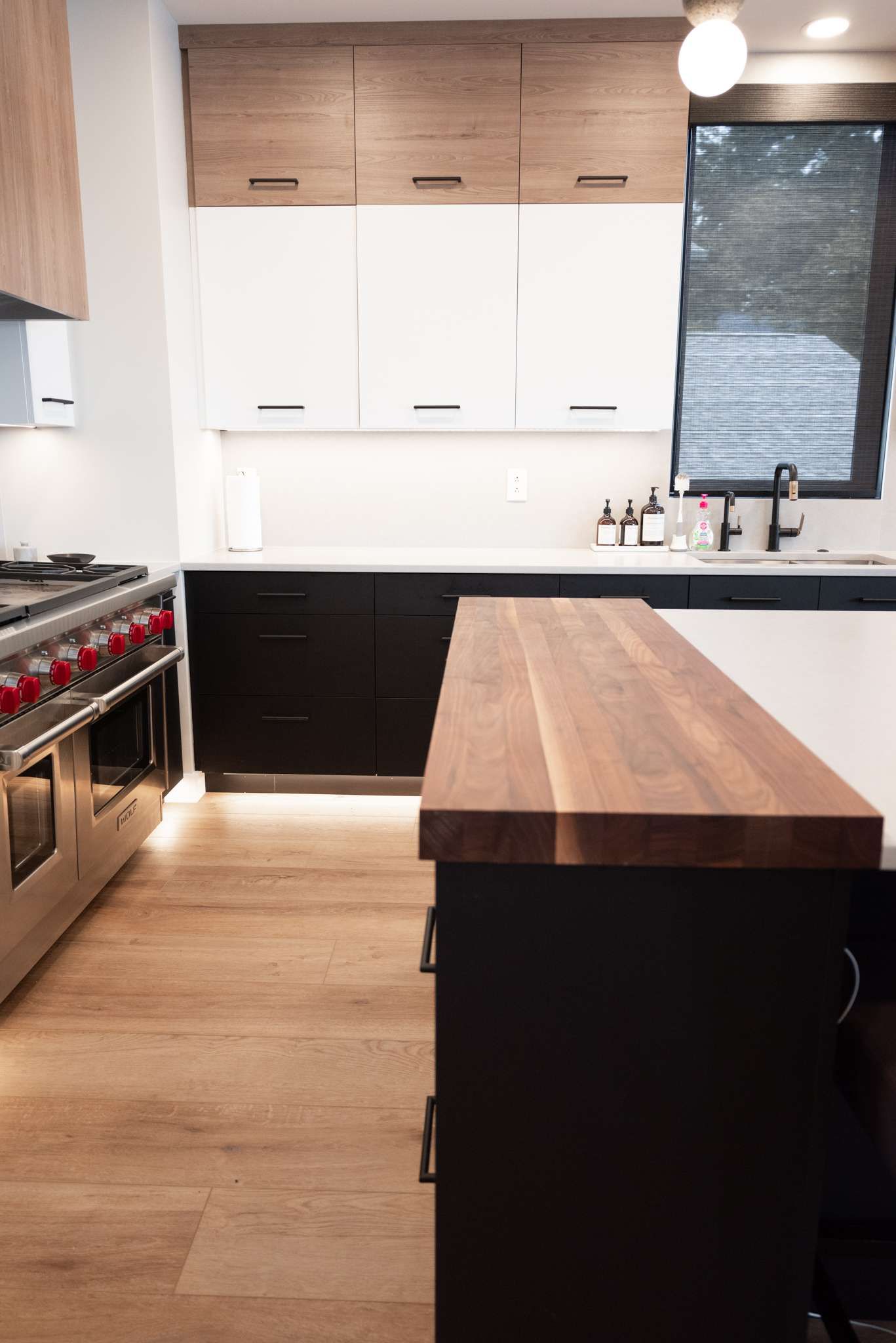 A kitchen with a wooden counter top , stove , oven , sink and window.