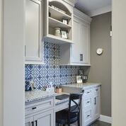 A kitchen with white cabinets , a sink , a desk and a chair.
