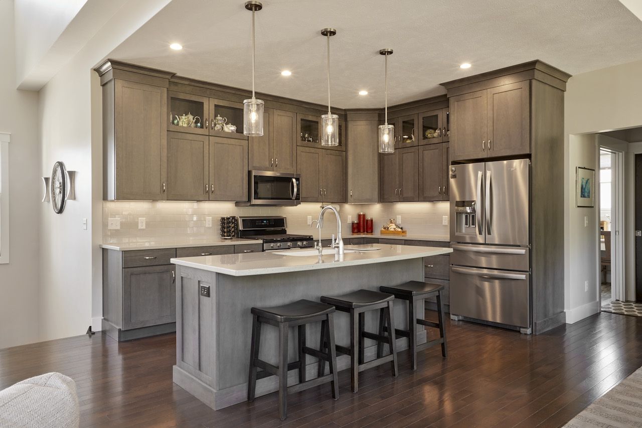 A kitchen with gray cabinets , stainless steel appliances , and a large island.