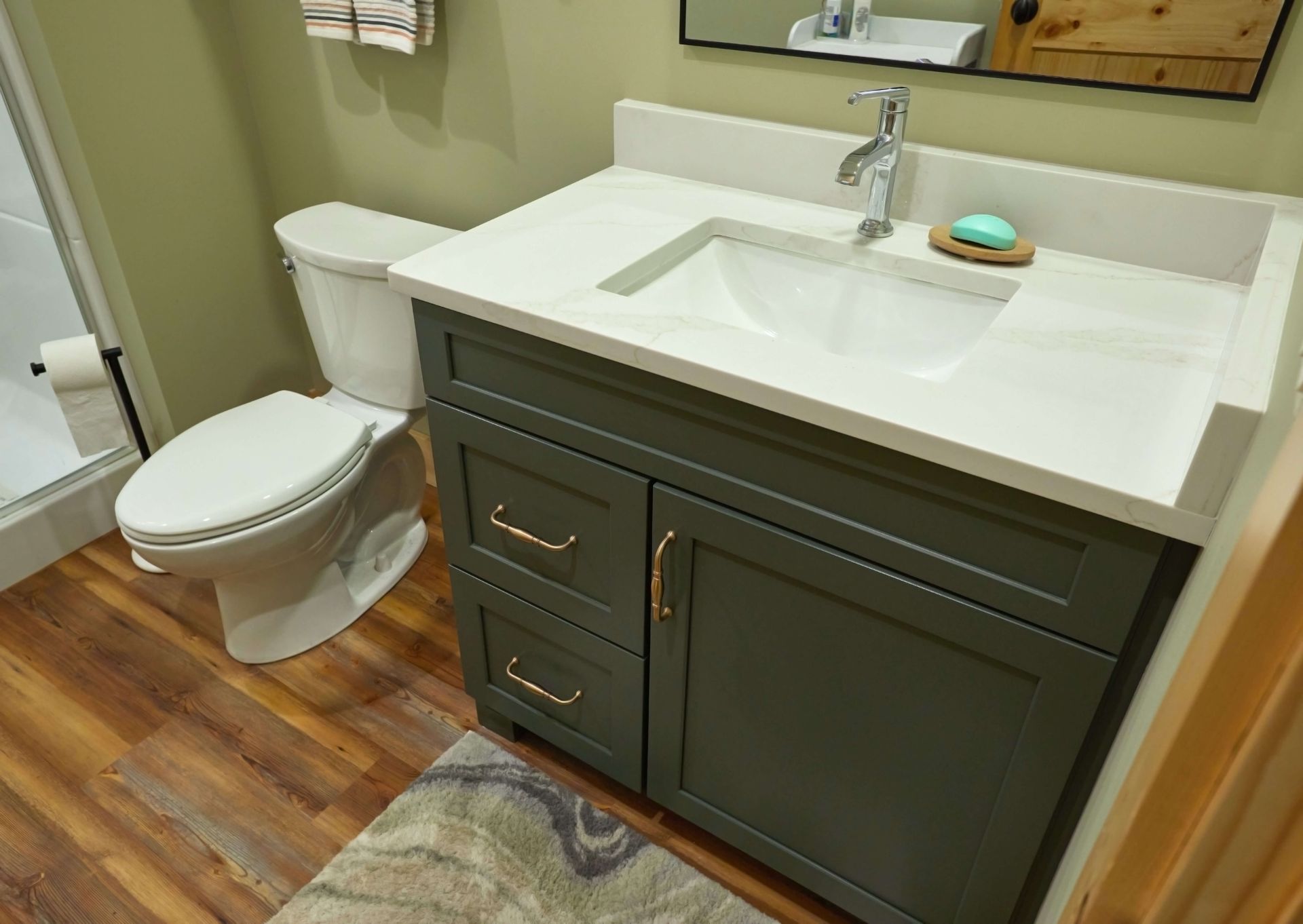 Bathroom with a toilet, sink, and green cabinet, on wood flooring, rug, and green wall.