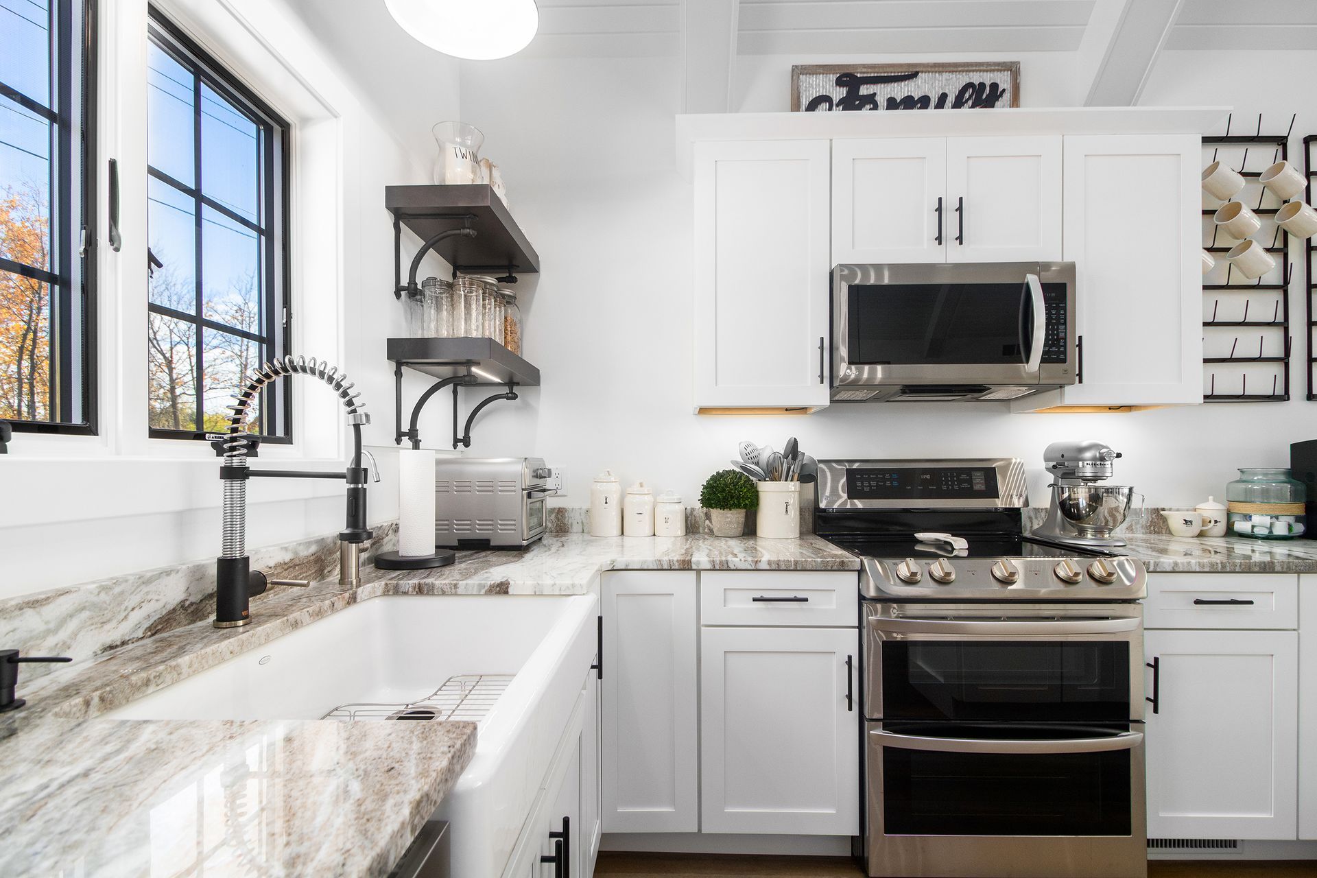 A kitchen with white cabinets , stainless steel appliances , a sink , and a microwave.