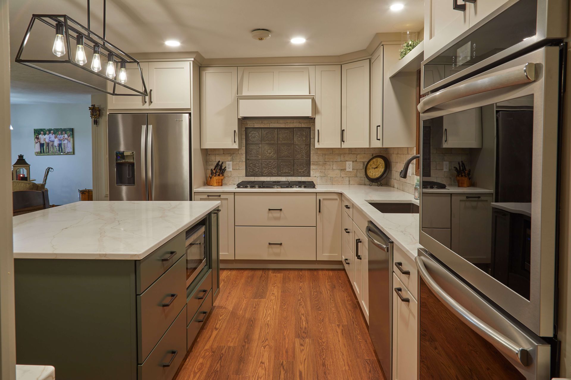 Modern kitchen with white cabinets, green island, stainless steel appliances, and wood floors.