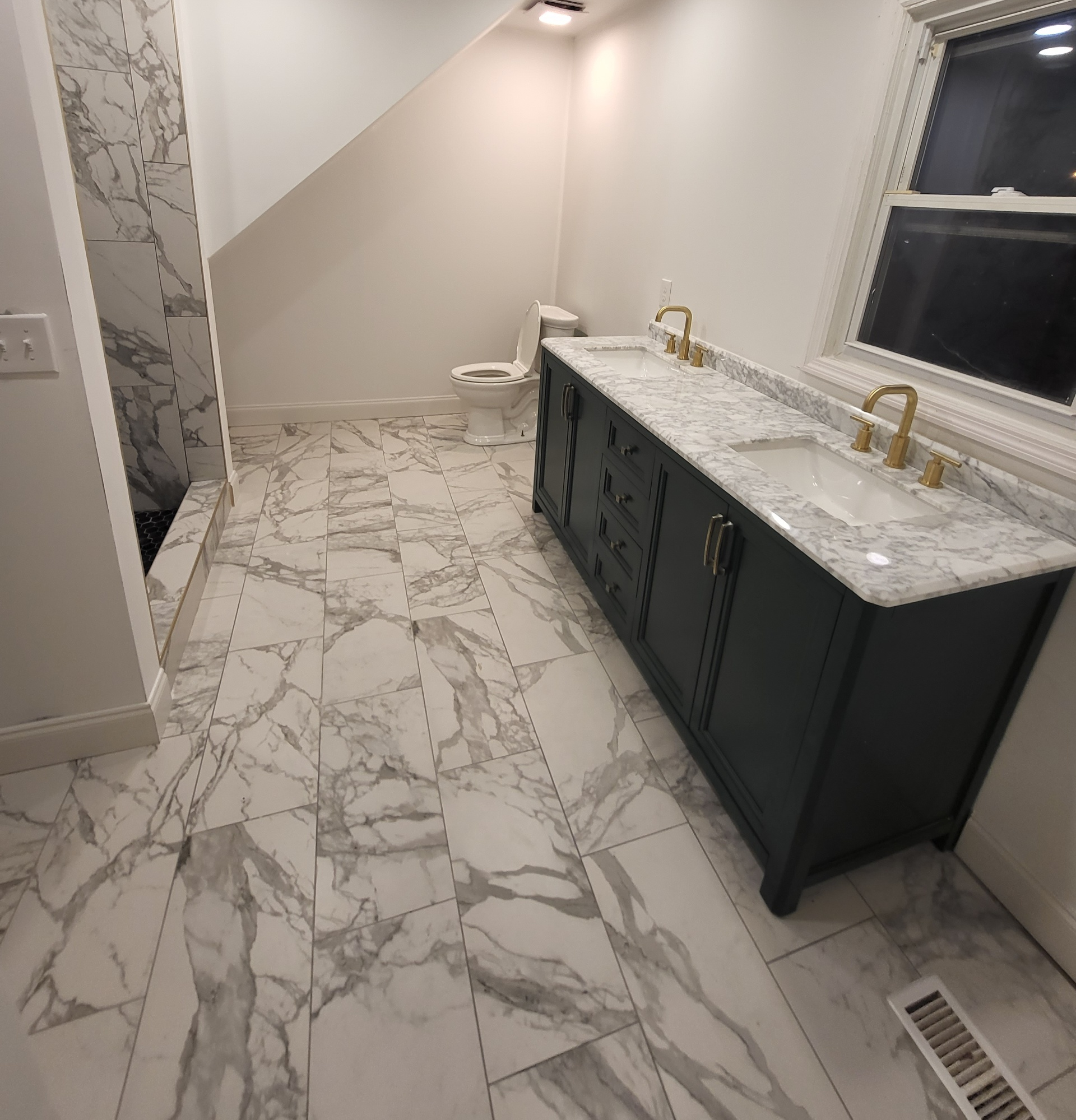 Bathroom with toilet, pedestal sink, round mirror, and gold fixtures; neutral walls and wood-look floor.