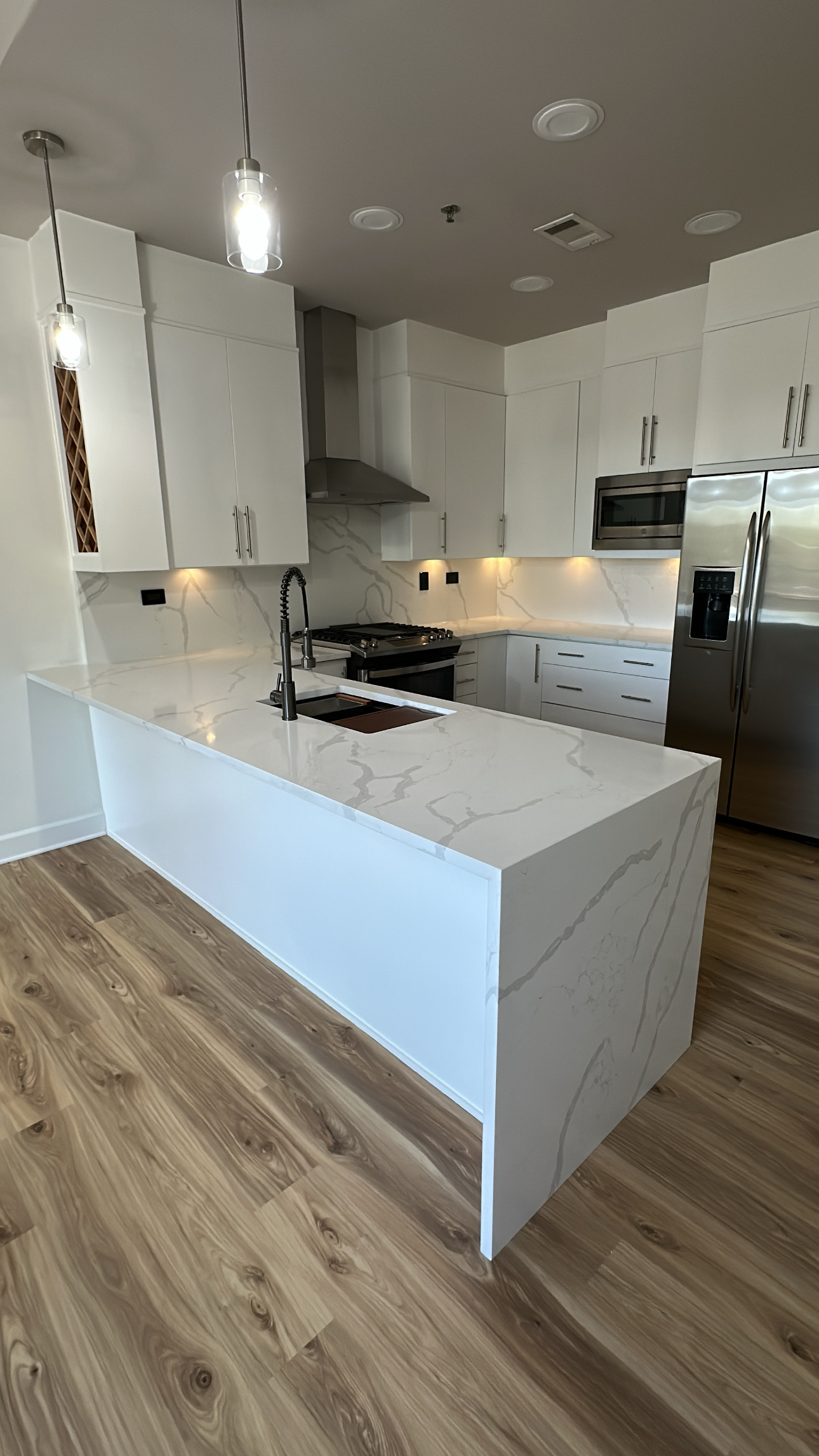 White kitchen cabinets with black hardware, sink, and cooktop. Stainless steel refrigerator.