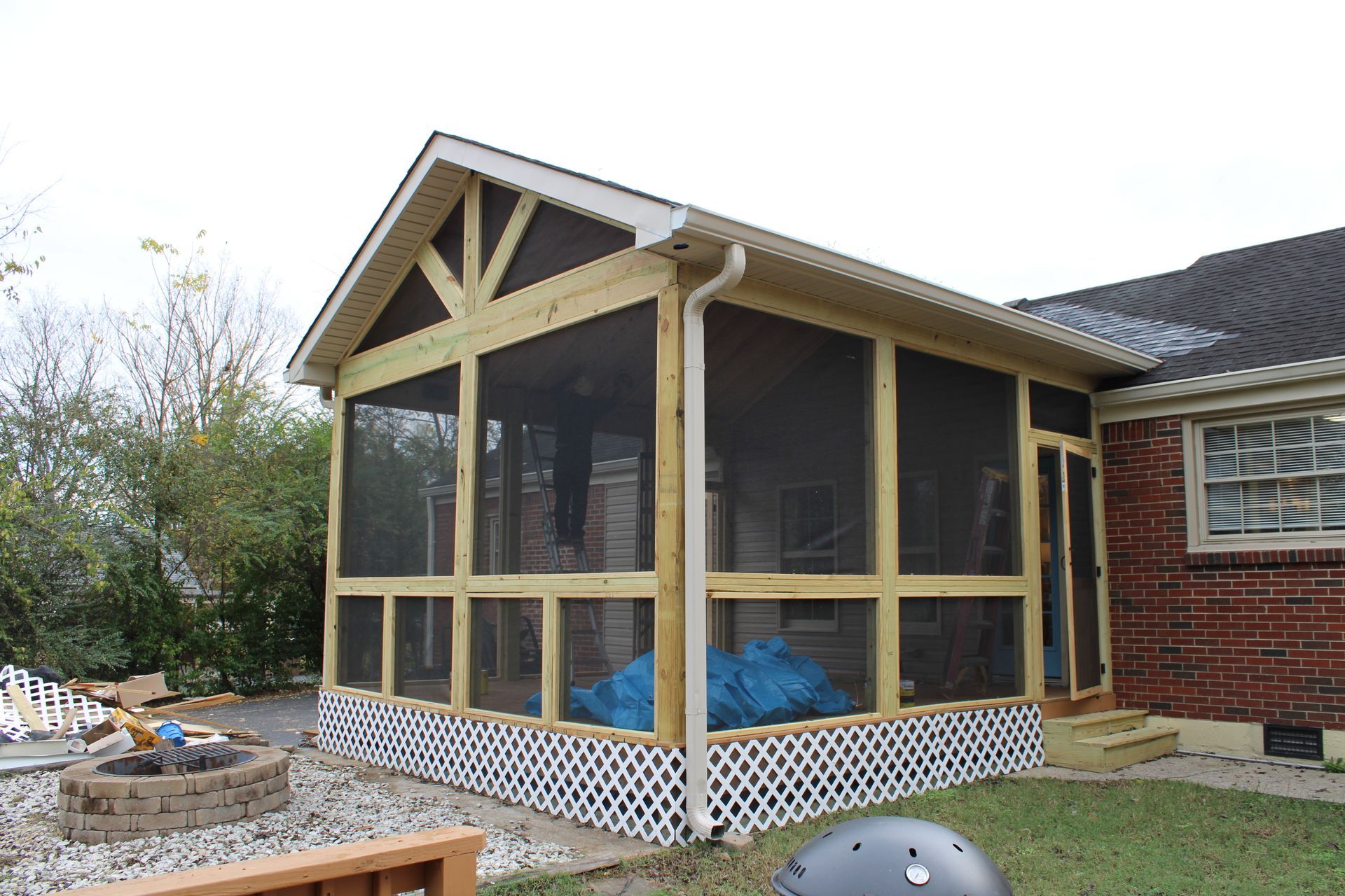 Screened porch addition with wooden frame and lattice base, attached to a brick house.