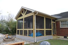 Screened porch addition with wooden frame and lattice base, attached to a brick house.