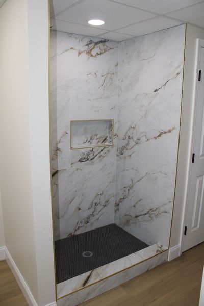 Walk-in shower with marble-like wall tile and dark stone floor, recessed shelf.