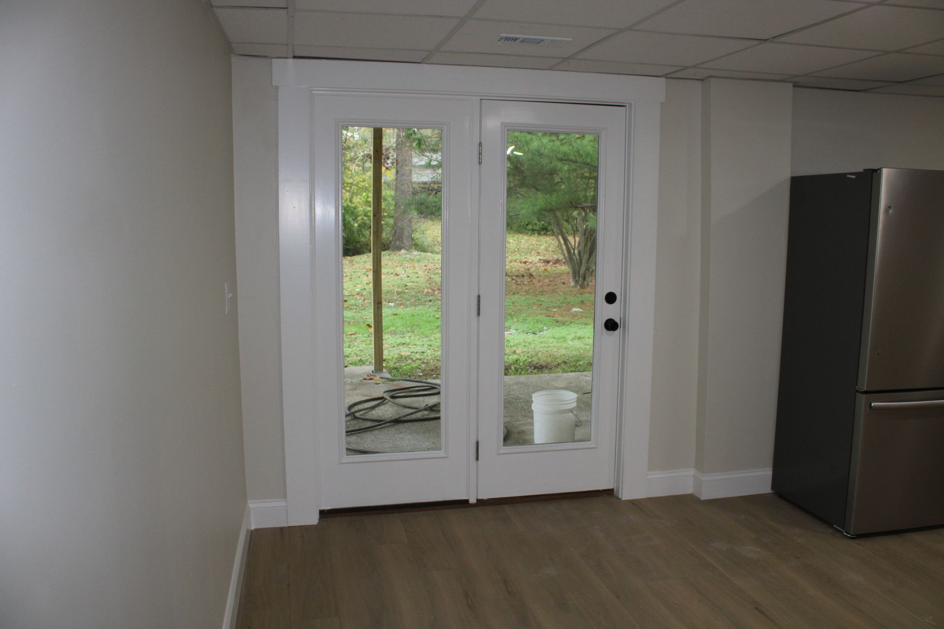 White French doors leading to a backyard. A refrigerator sits to the right of the doors.
