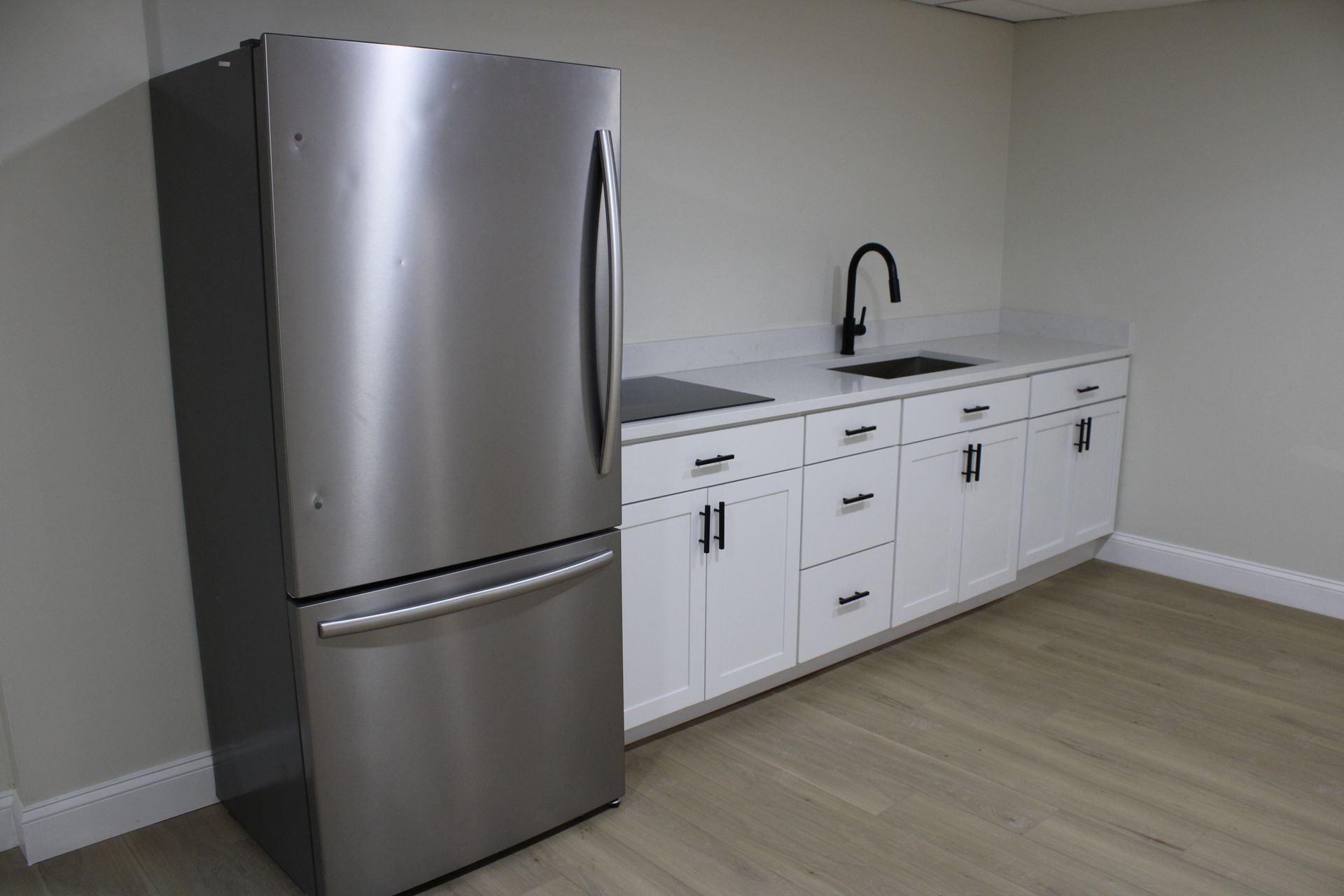 Stainless steel refrigerator next to white cabinets with black hardware and a sink.