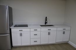 White kitchen cabinets with black hardware, sink, and cooktop. Stainless steel refrigerator.