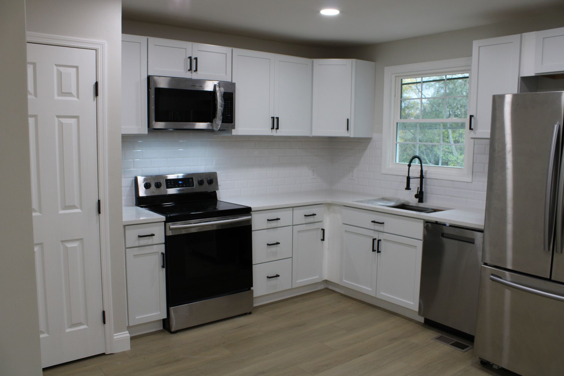 White kitchen with stainless steel appliances, white cabinets, and light wood flooring.