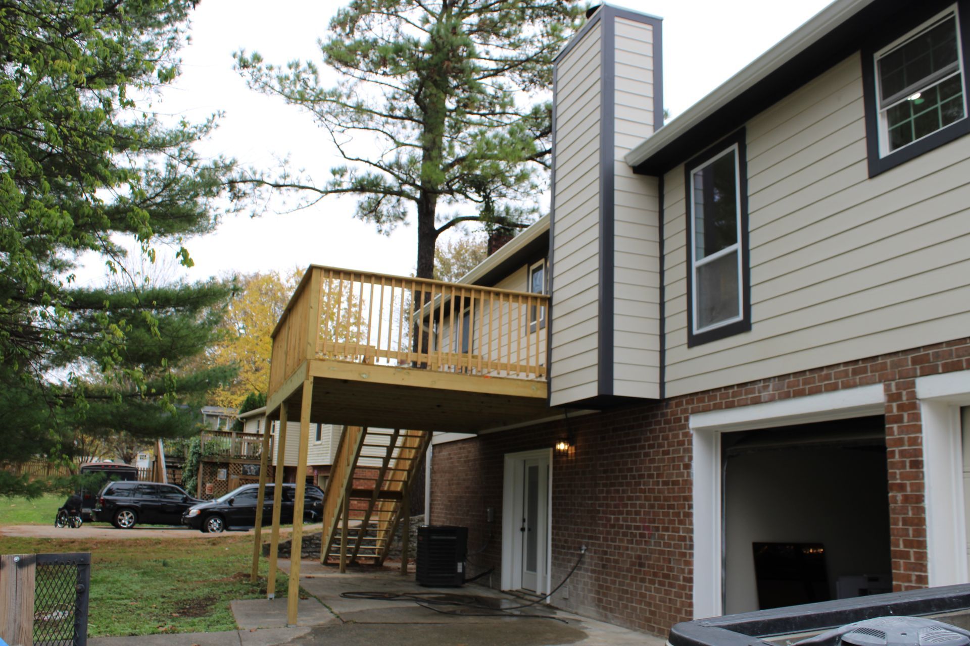 Two-story building with a wooden deck. Brick base, beige siding, black trim, and stairs leading to the deck.