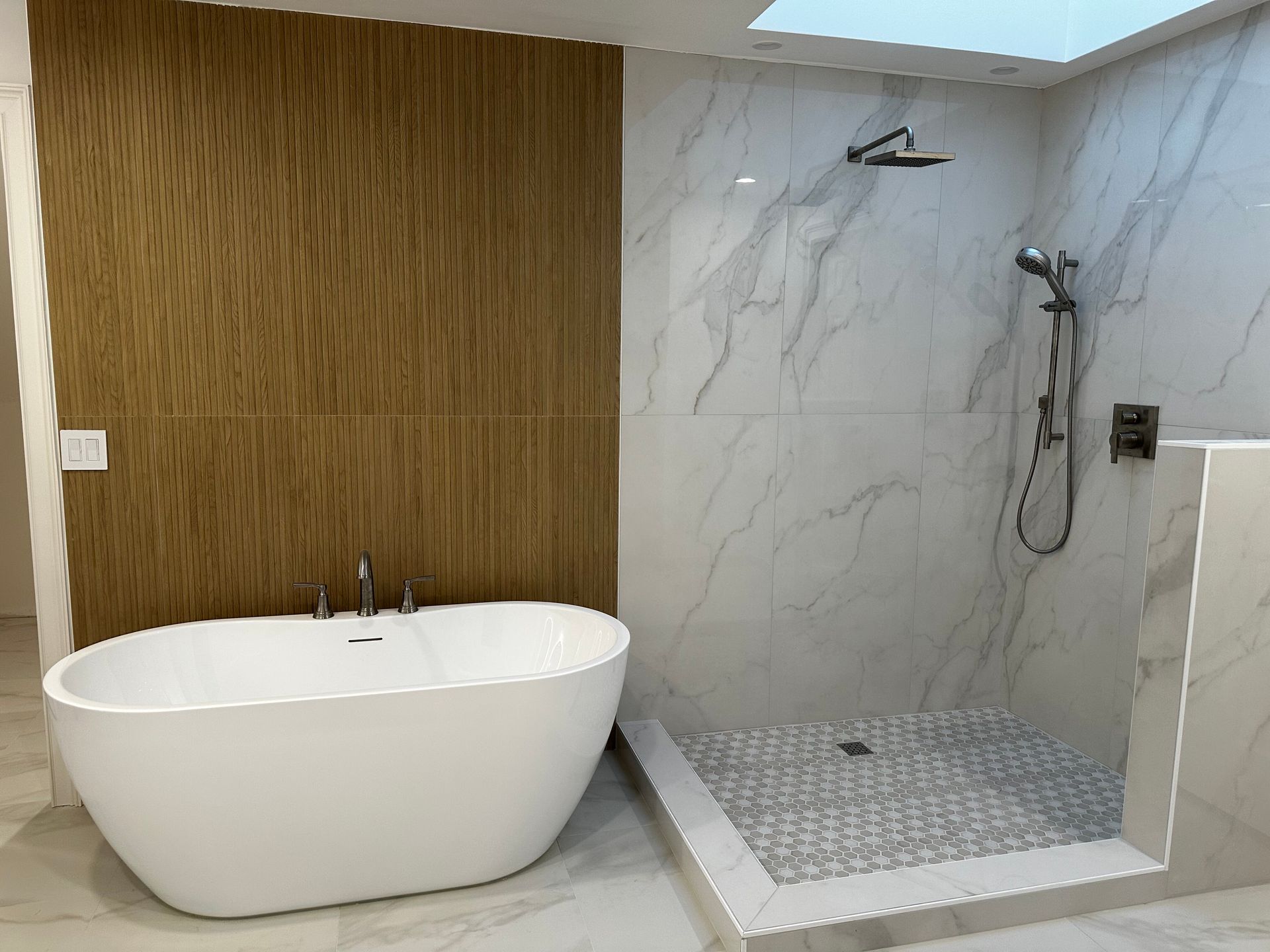 Bathroom with toilet, pedestal sink, round mirror, and gold fixtures; neutral walls and wood-look floor.