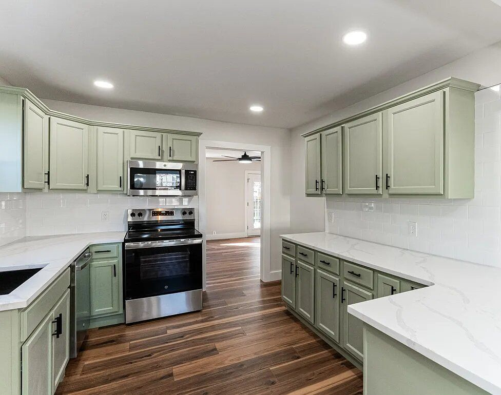 White kitchen cabinets with black hardware, sink, and cooktop. Stainless steel refrigerator.