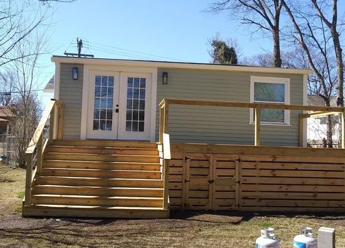 Wooden deck with stairs leading to a light green building with white double doors and a window.