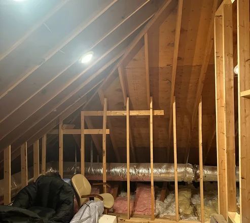Wooden attic under construction with exposed beams, insulation, and ductwork.