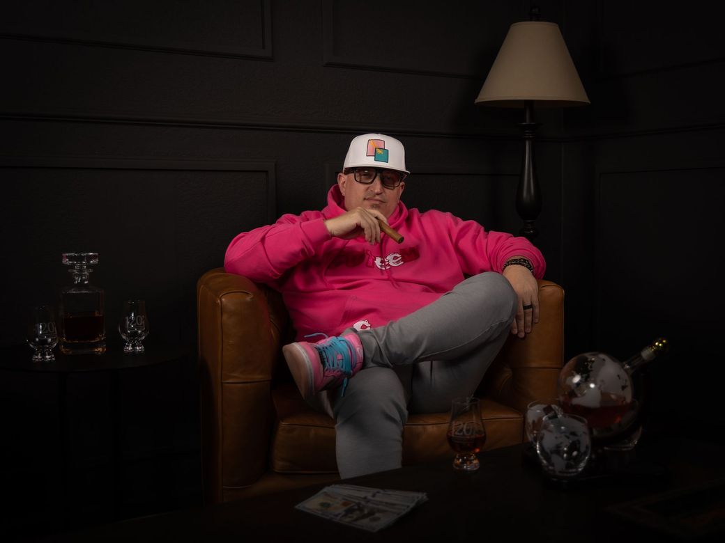 A man in a pink hoodie is sitting in a chair with his legs crossed.