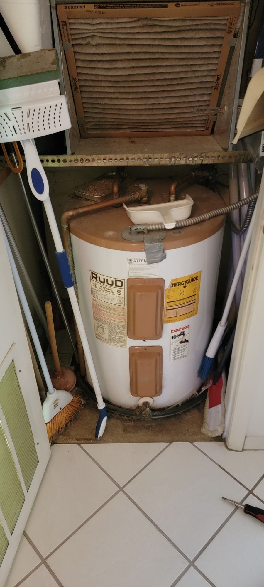 A water heater is sitting under a shelf in a closet.