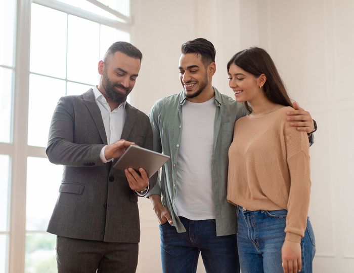 A man is holding a tablet while standing next to a man and woman.