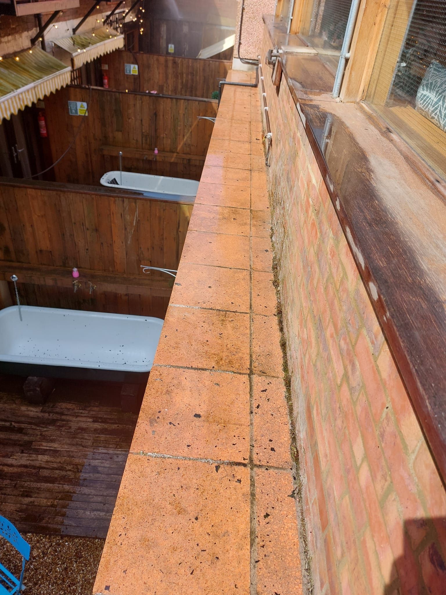 A bathtub is sitting on the edge of a brick wall next to a window.