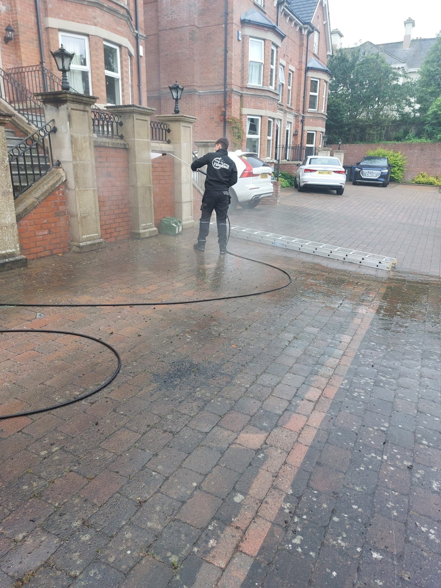 A man is cleaning a brick driveway with a high pressure washer.