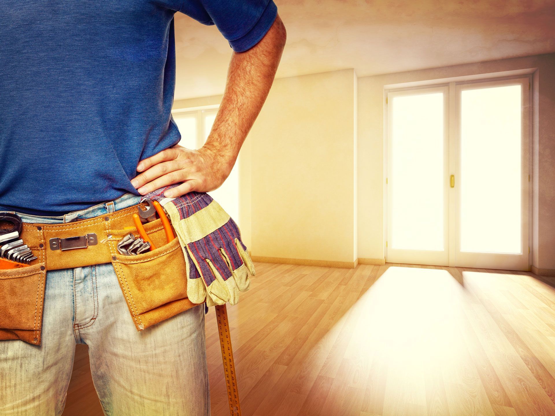 A man wearing a tool belt and gloves is standing in an empty room .