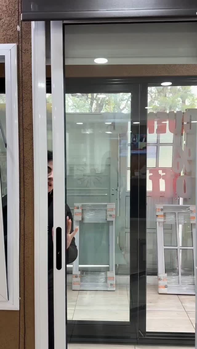 Persona abriendo una puerta corrediza de vidrio, marco blanco, manija negra, mostrando un entorno al aire libre.