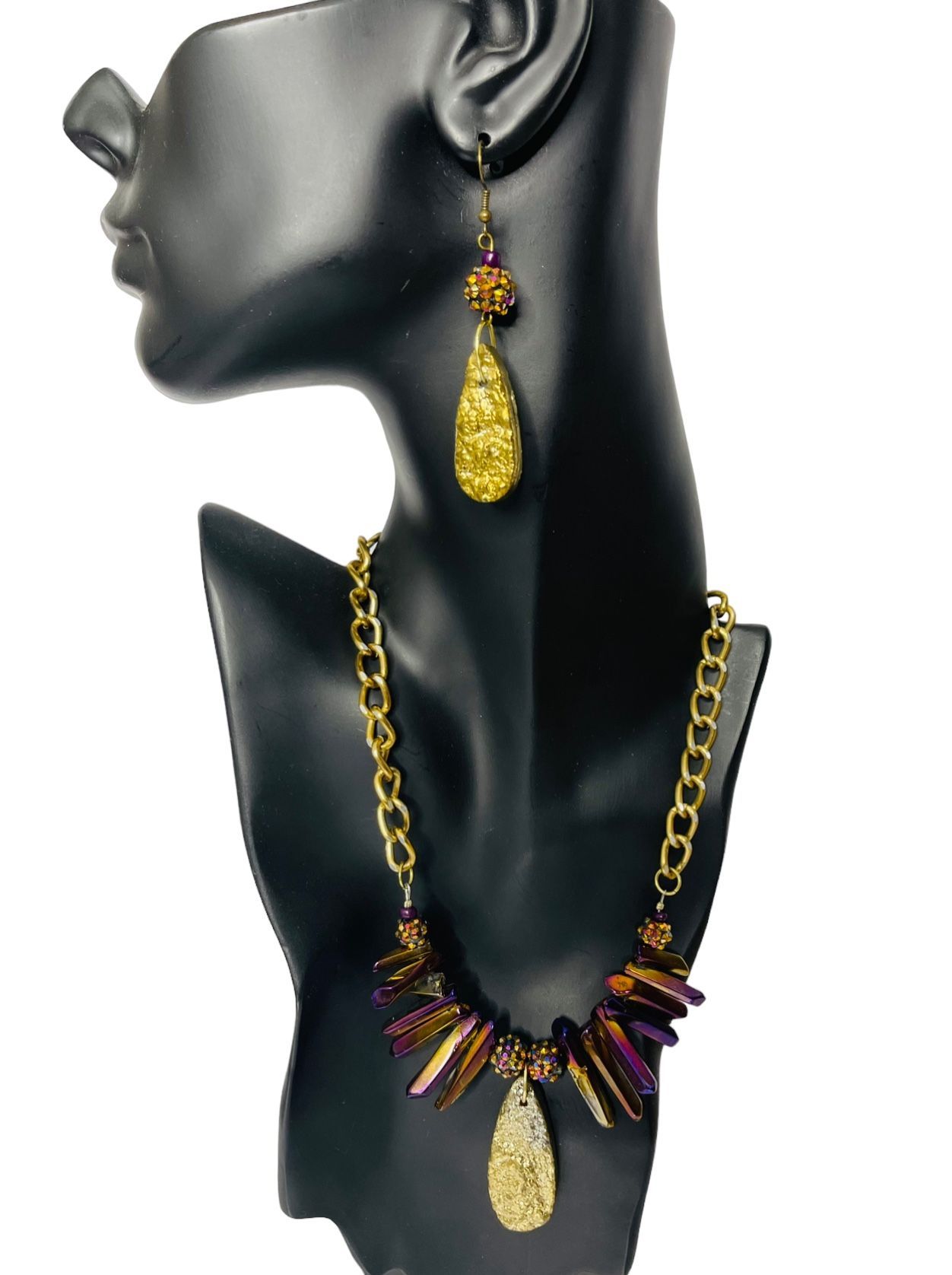 Gold necklace and earrings set on a black mannequin, featuring purple and gold accents.