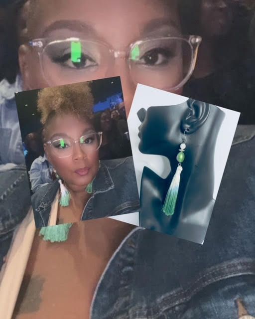 Woman in glasses, wearing earrings and denim jacket, holding pictures of herself wearing the same earrings.