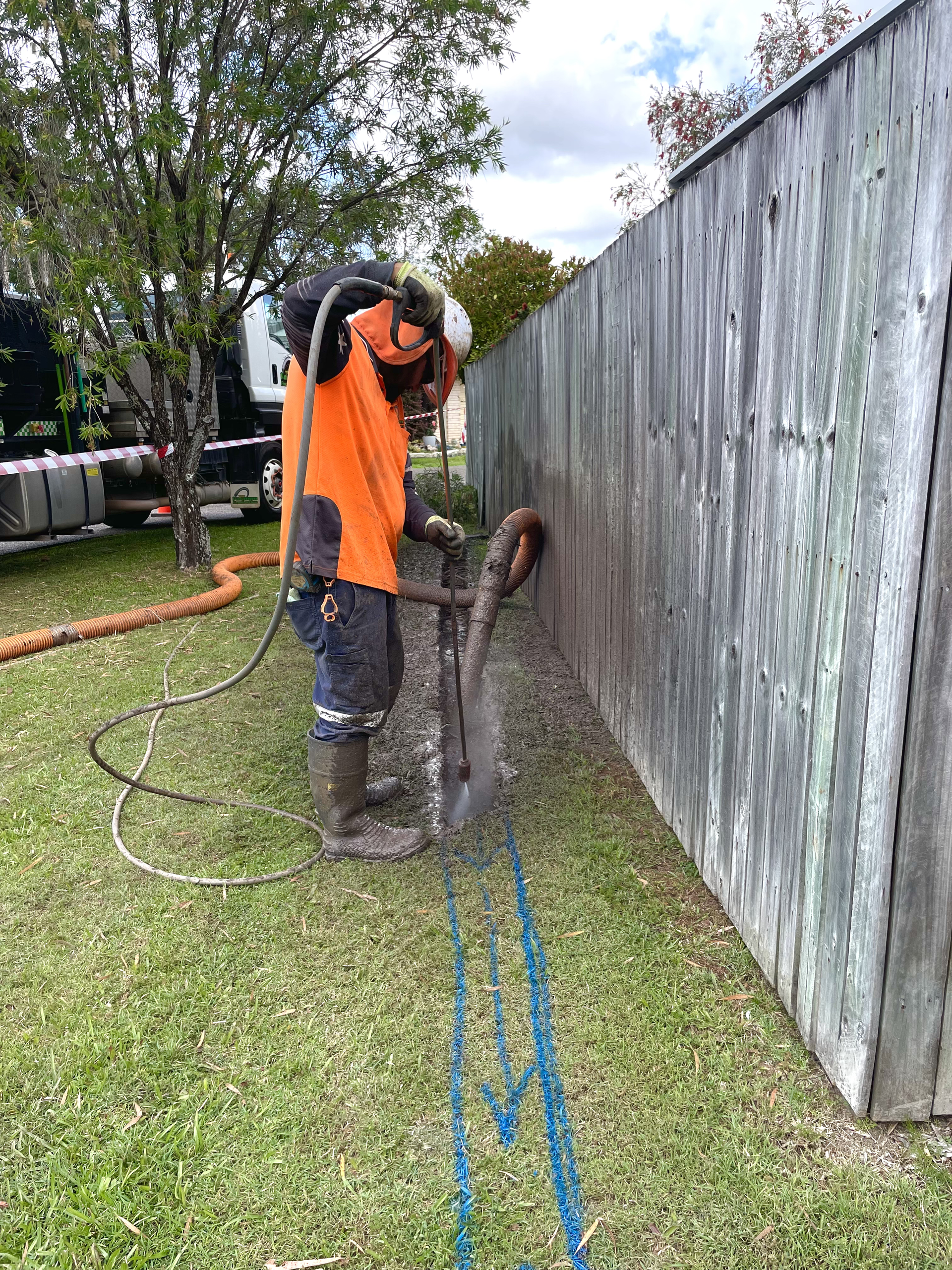 A Man Is Cutting A Hole In A Fence With A Drill — Tyzac Vacuum Excavation in Sunshine Coast, QLD