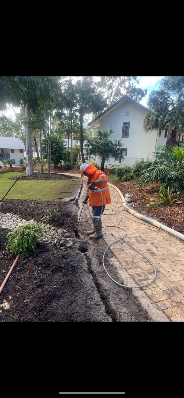 A Man Is Digging A Hole In The Ground In Front Of A House — Tyzac Vacuum Excavation in North Brisbane, QLD