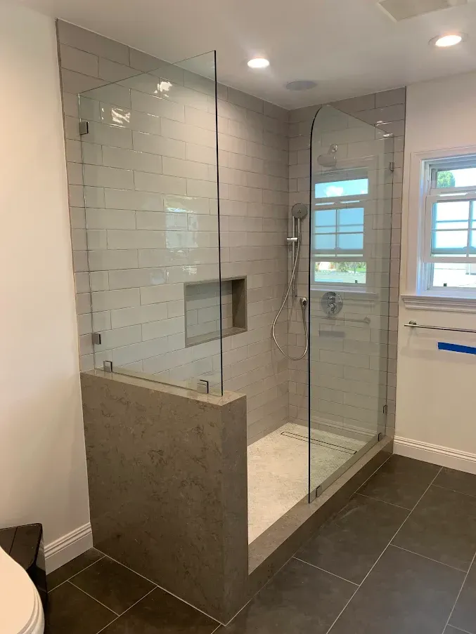 Glass shower enclosure in a white bathroom, with a window to the left.