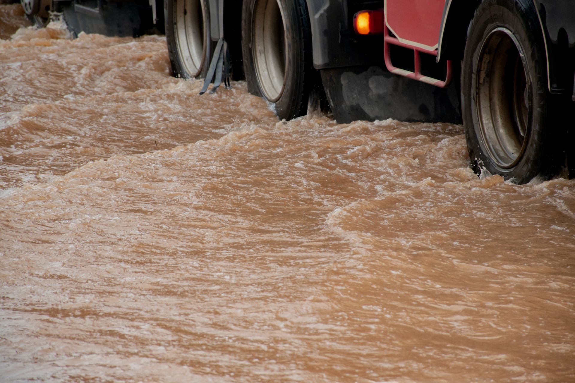 Truck tires submerged in muddy, flowing water, possibly during a flood.