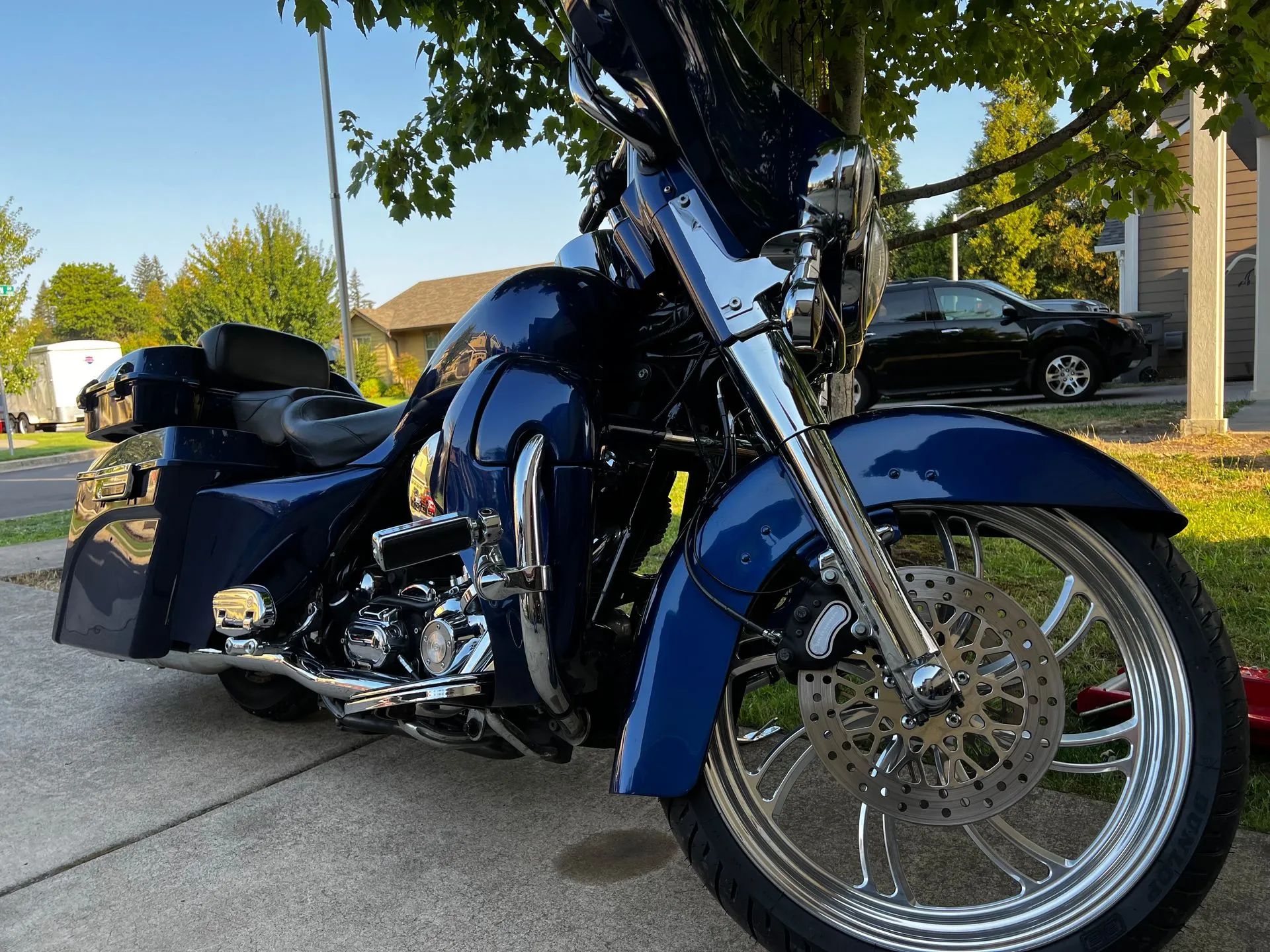 A blue harley davidson motorcycle is parked on the sidewalk in front of a house.
