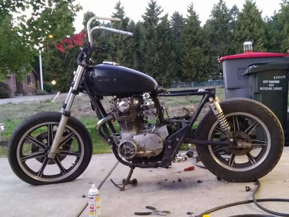 A black motorcycle is parked on a sidewalk next to a trash can that says recycling