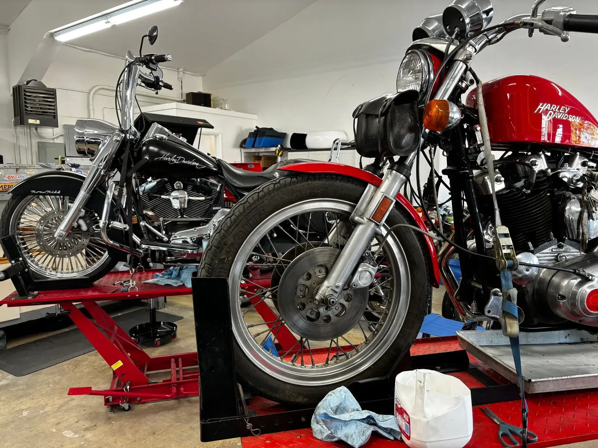 Two motorcycles are sitting on a lift in a garage.