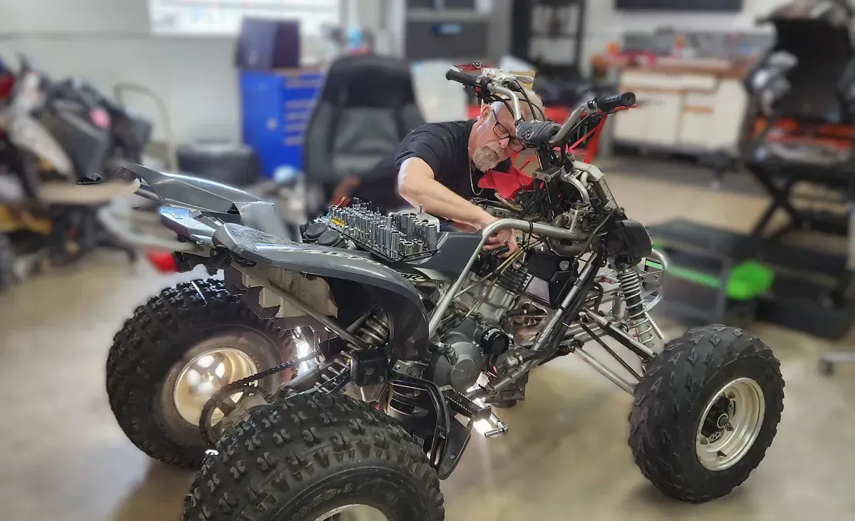 A man is working on a four wheeler in a garage.