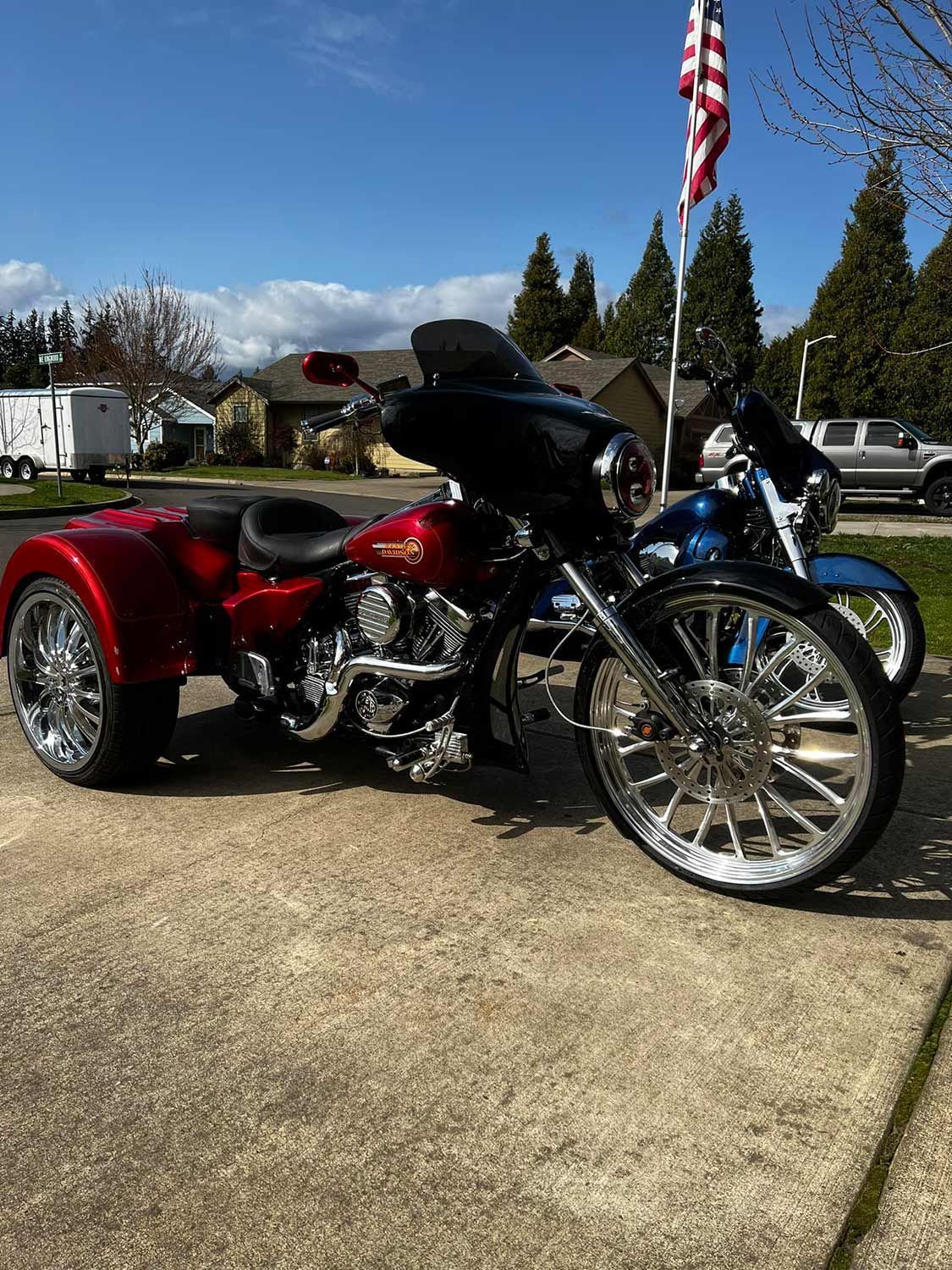 A red motorcycle with three wheels is parked next to a blue motorcycle.