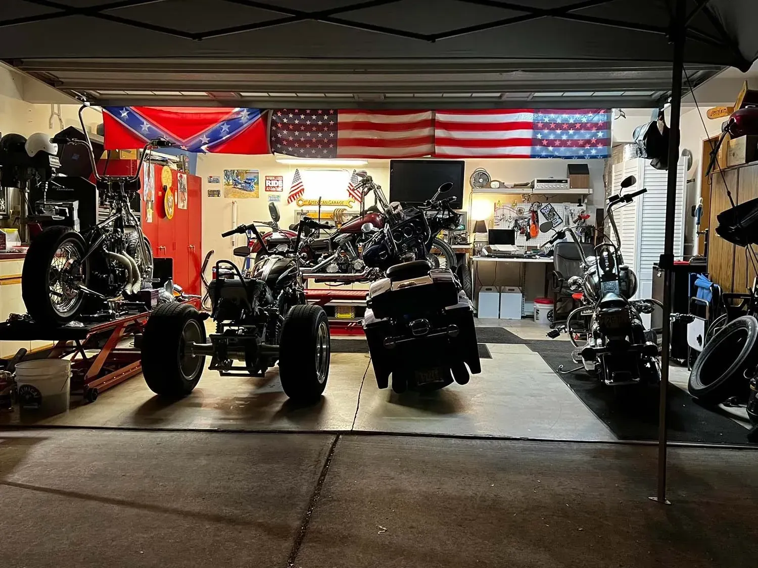 Several motorcycles are parked in a garage with an american flag in the background