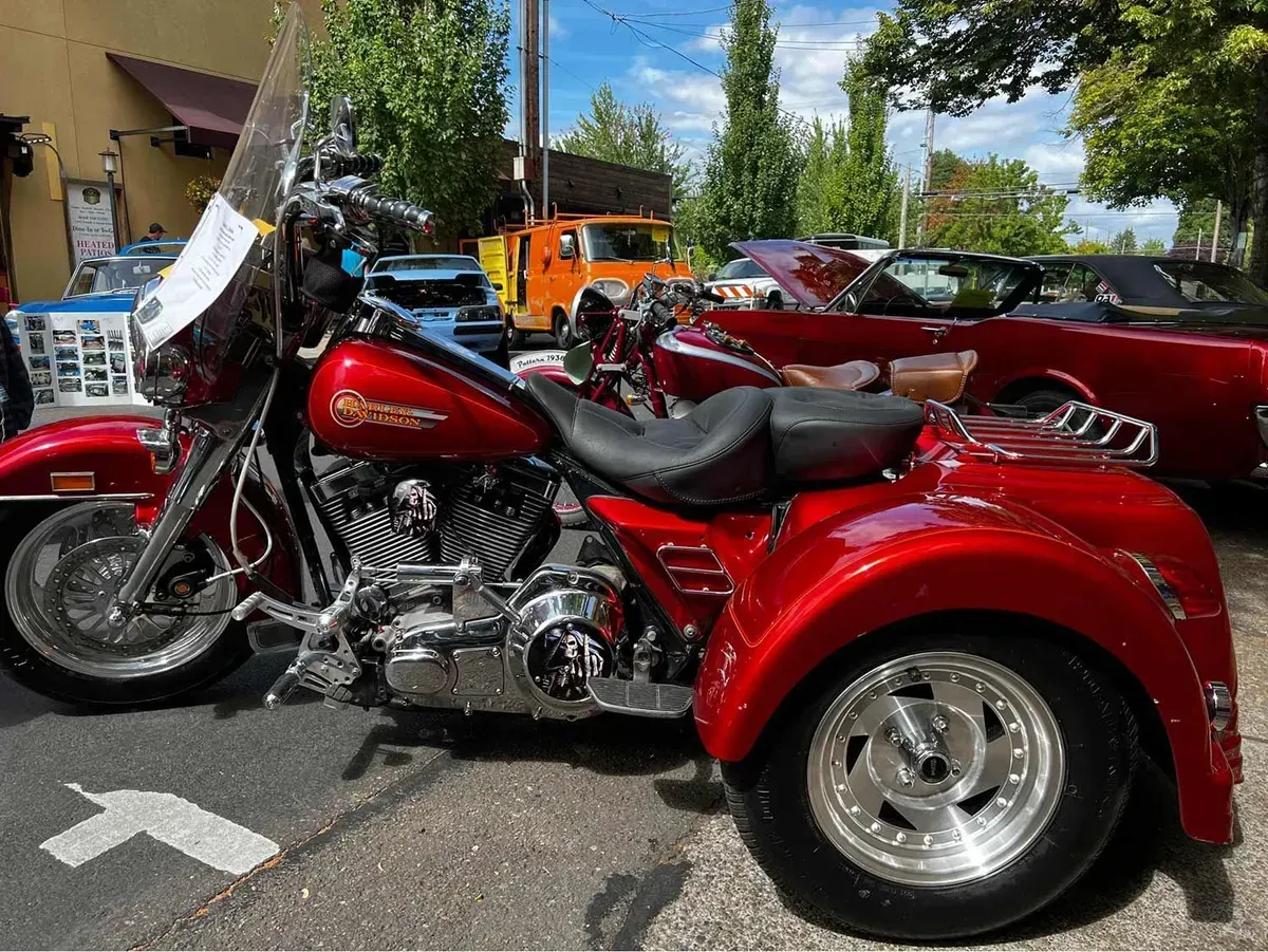 A red motorcycle with three wheels is parked in a parking lot.